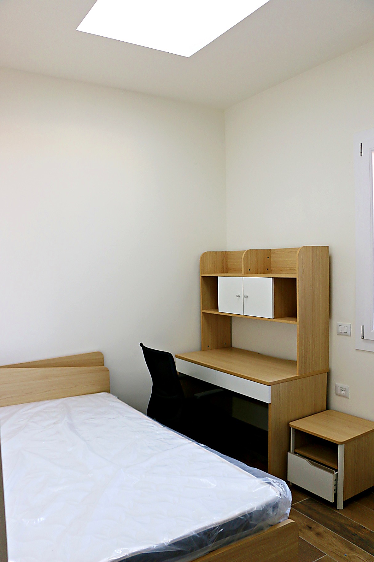 Single room bed and desk under a skylight